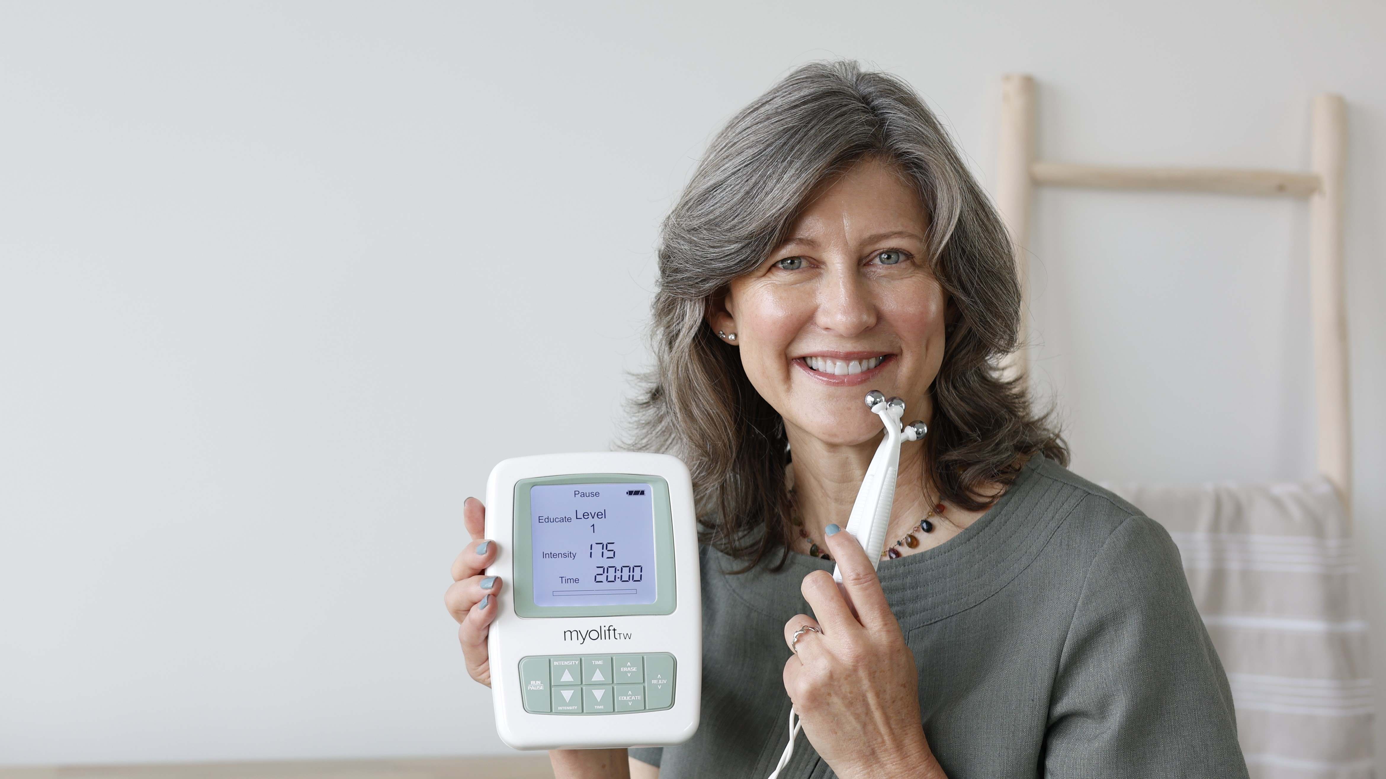 middle aged women sits in front of a dresser with a microcurrent device sitting on top
