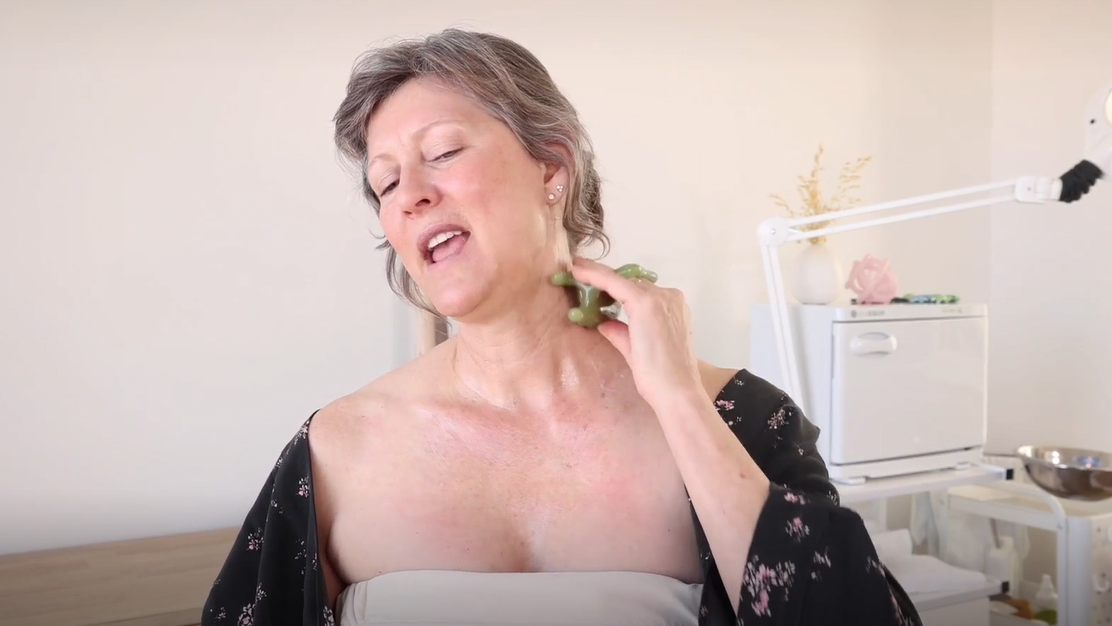 A middle aged woman massages her neck with a massage tool